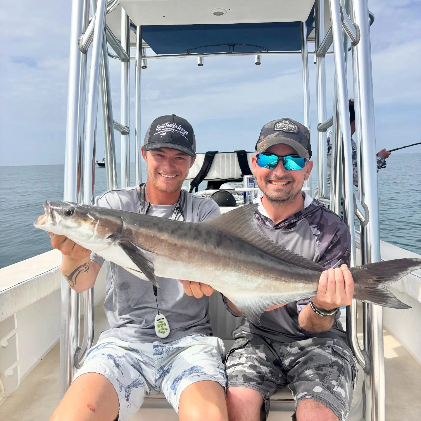 Anglers holding a freshly caught cobia aboard a fly fishing charter boat in Sarasota Bay.