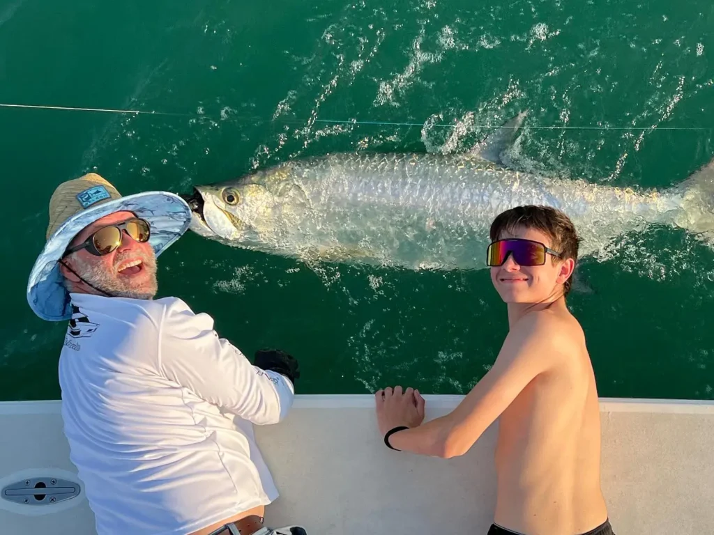 Young angler and captain releasing a tarpon beside a Sarasota fishing charter boat.