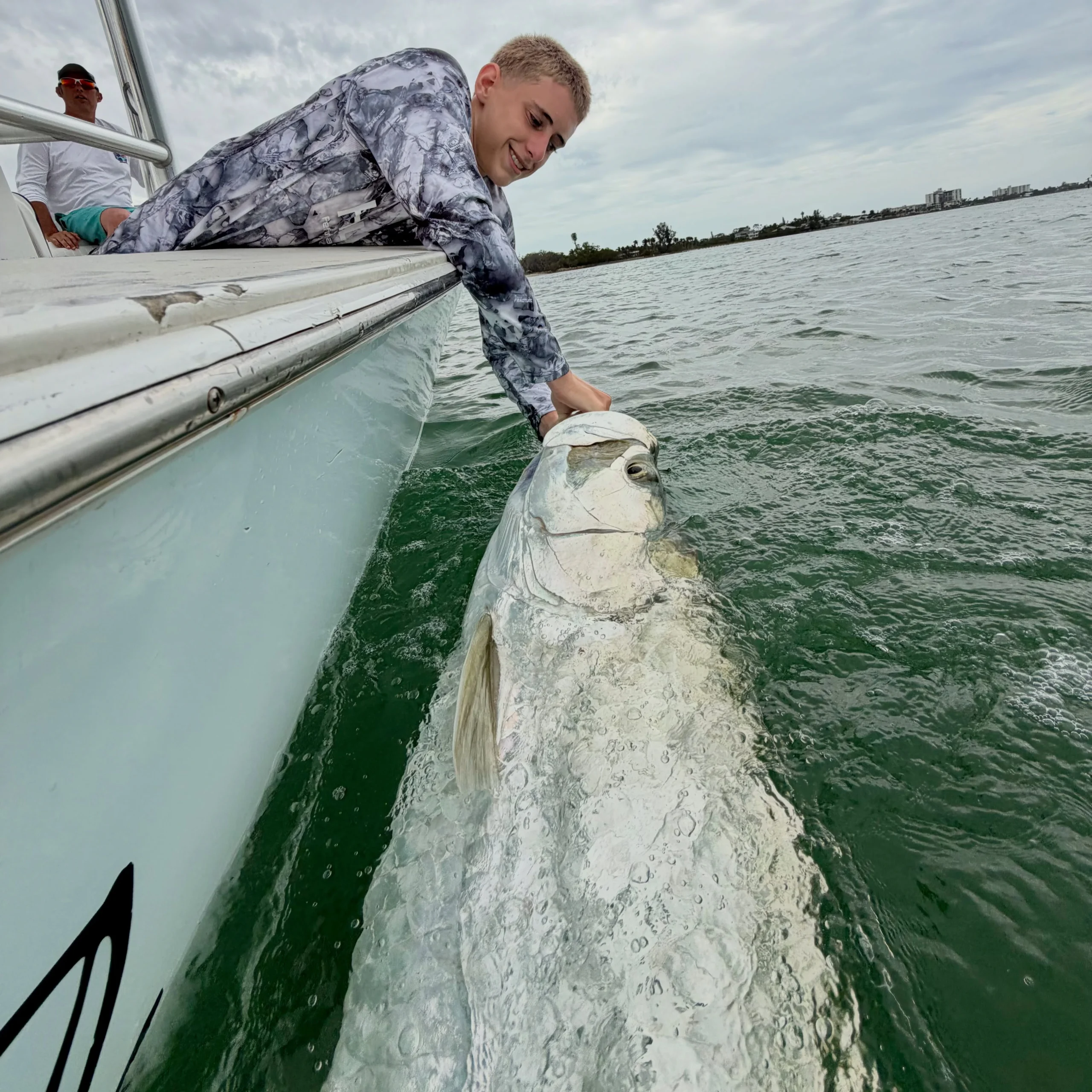 Young angler releasing a trophy tarpon beside the boat after a successful Sarasota fly fishing charter.
