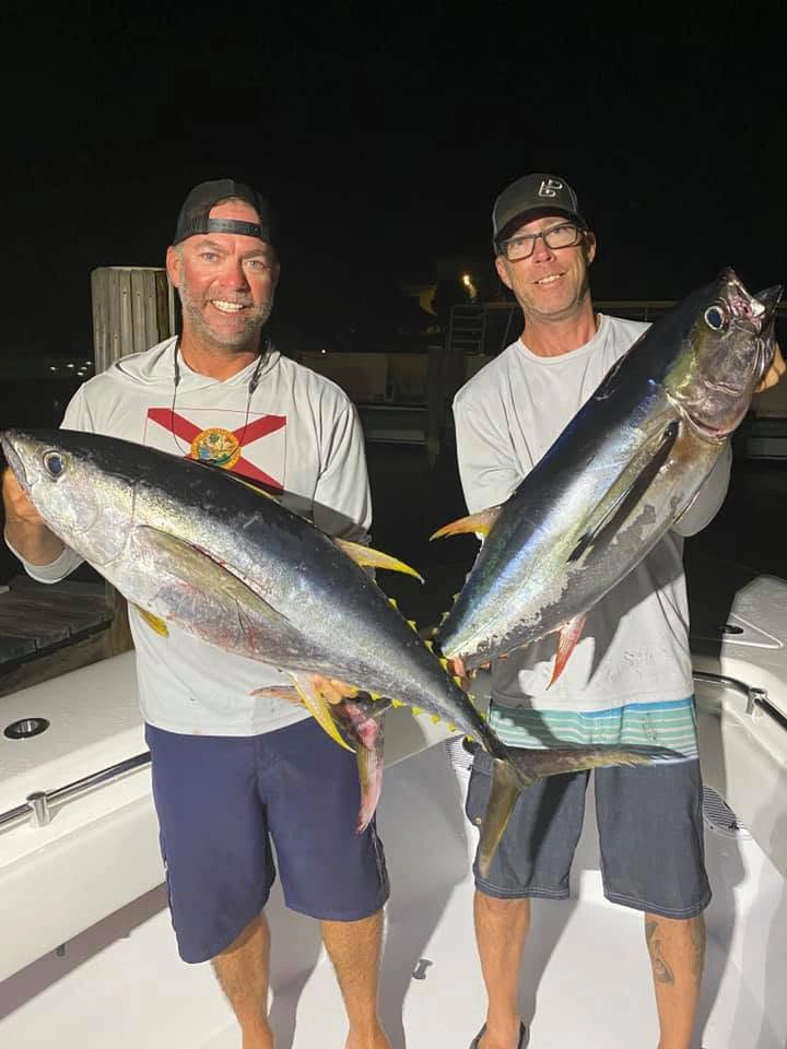 Two anglers holding freshly caught blackfin tuna during a nighttime offshore fishing charter out of Sarasota, Florida.