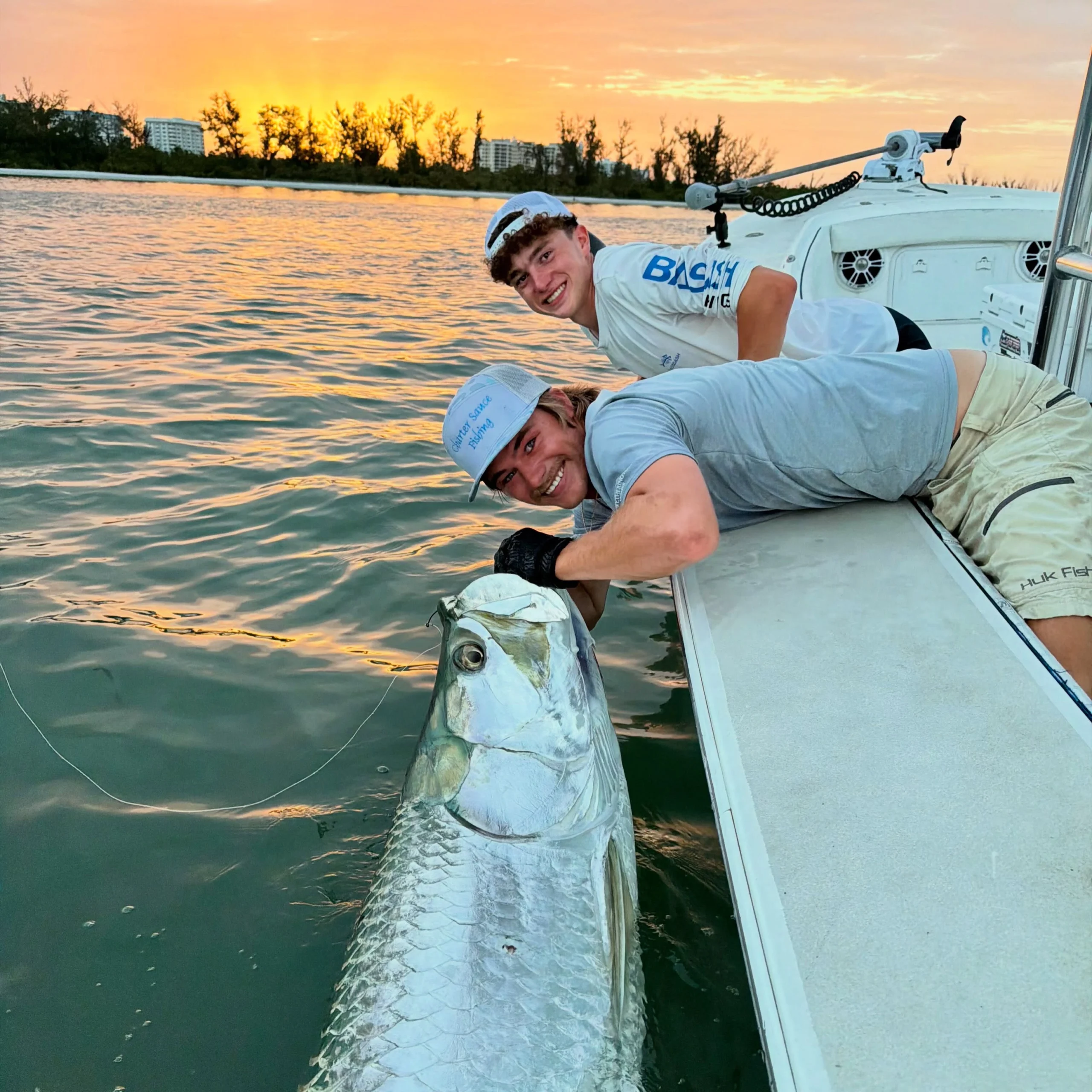Young captain landing a large tarpon beside the boat during a Sarasota fishing charter at sunset.