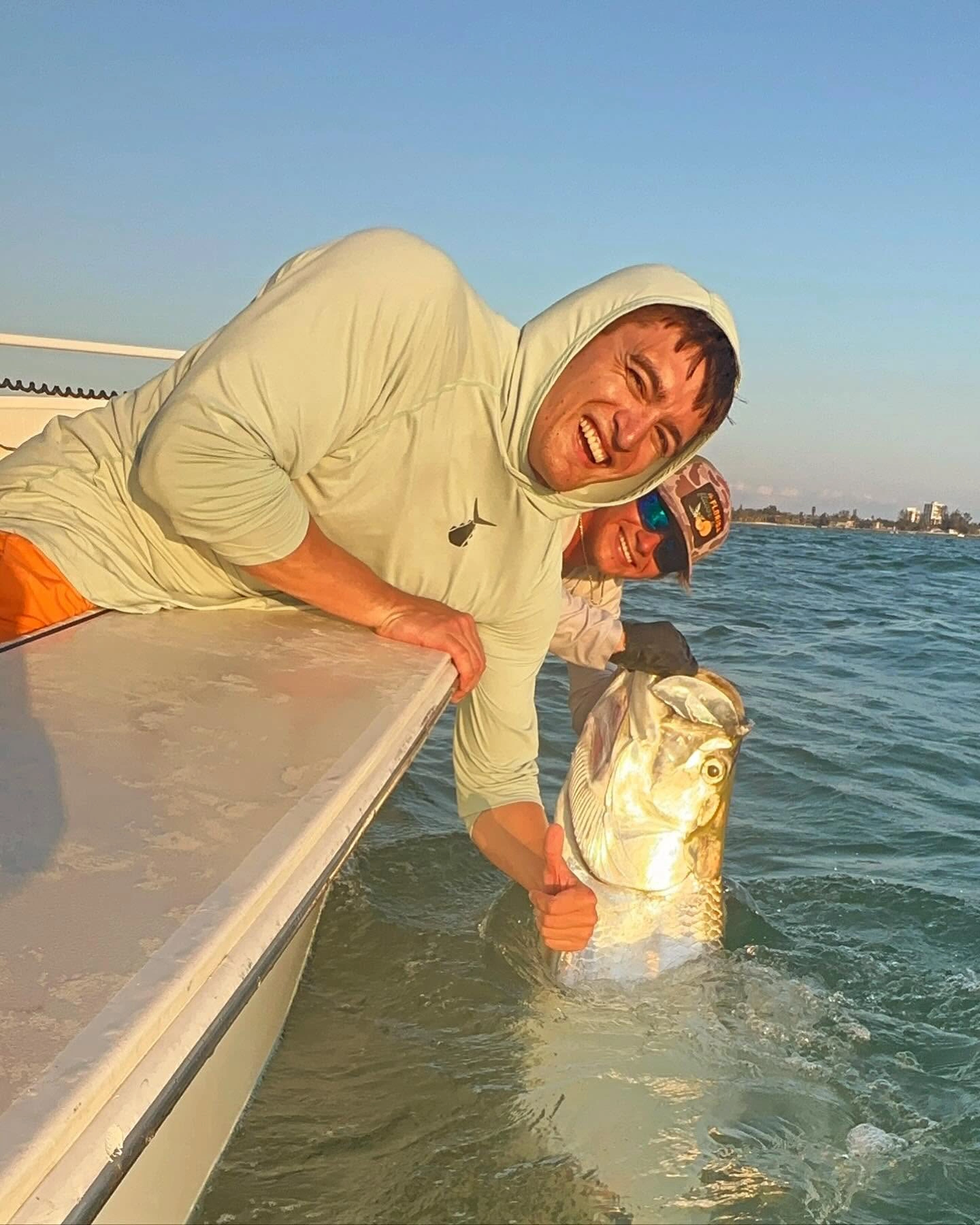 Young angler smiling beside a large tarpon in the water while the captain prepares for a safe release during a Sarasota fishing charter.