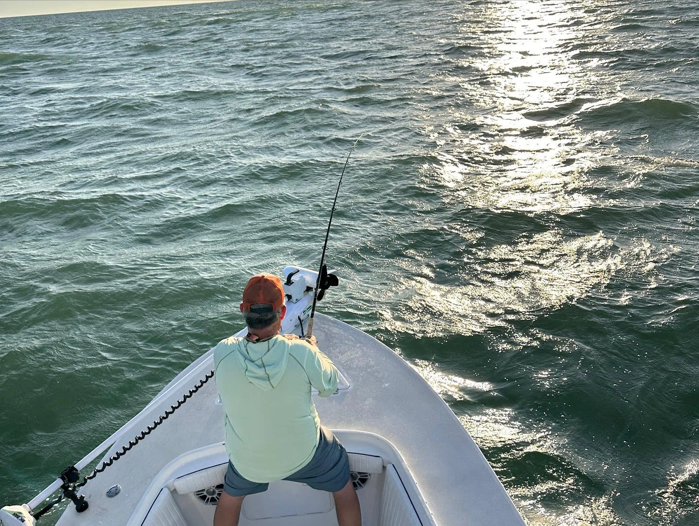Angler fighting a powerful fish from the bow of a Sarasota fishing charter boat during golden hour on Sarasota Bay.