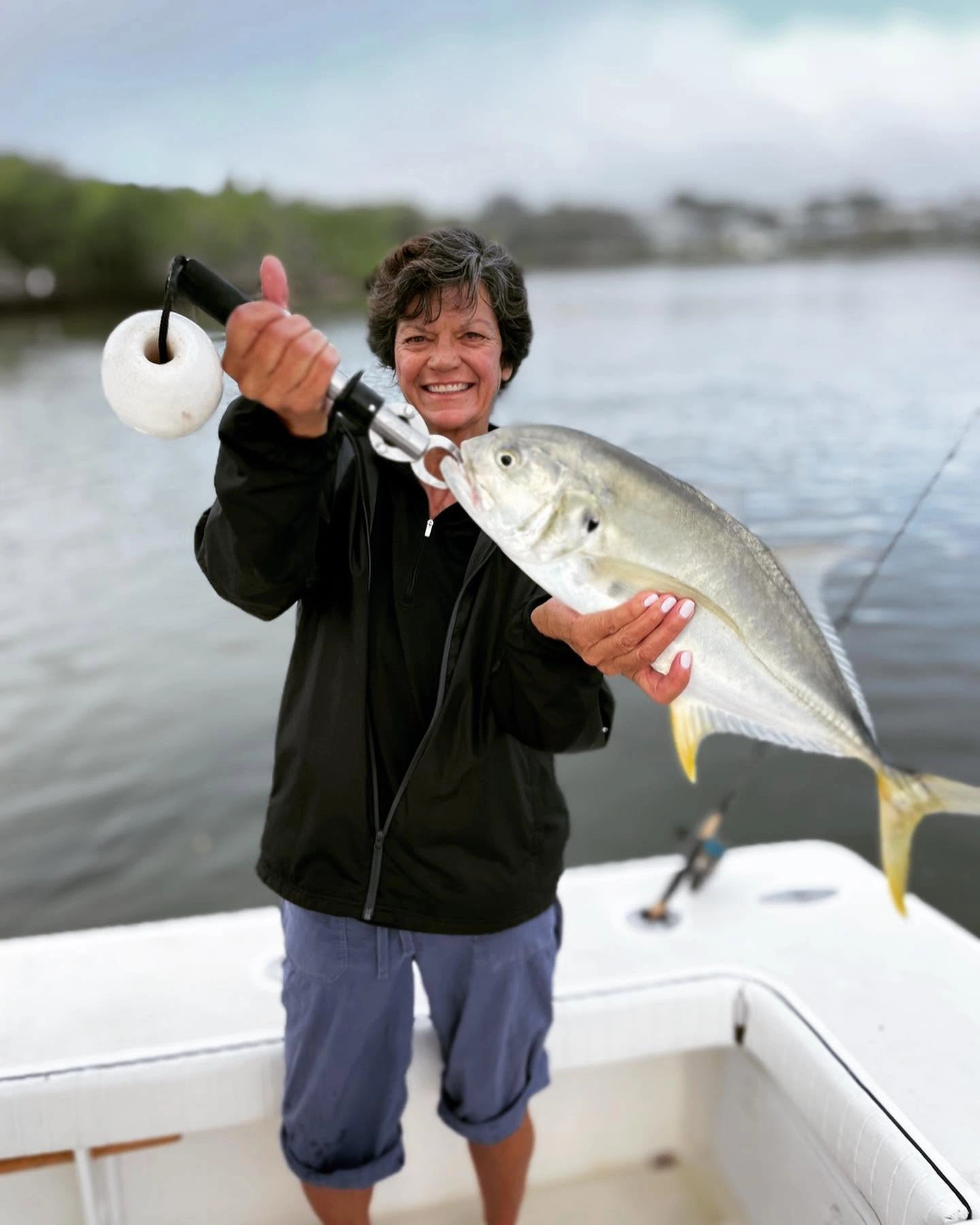 Smiling angler holding a jack crevalle with a fish gripper during a Sarasota inshore fishing charter on calm backwaters.