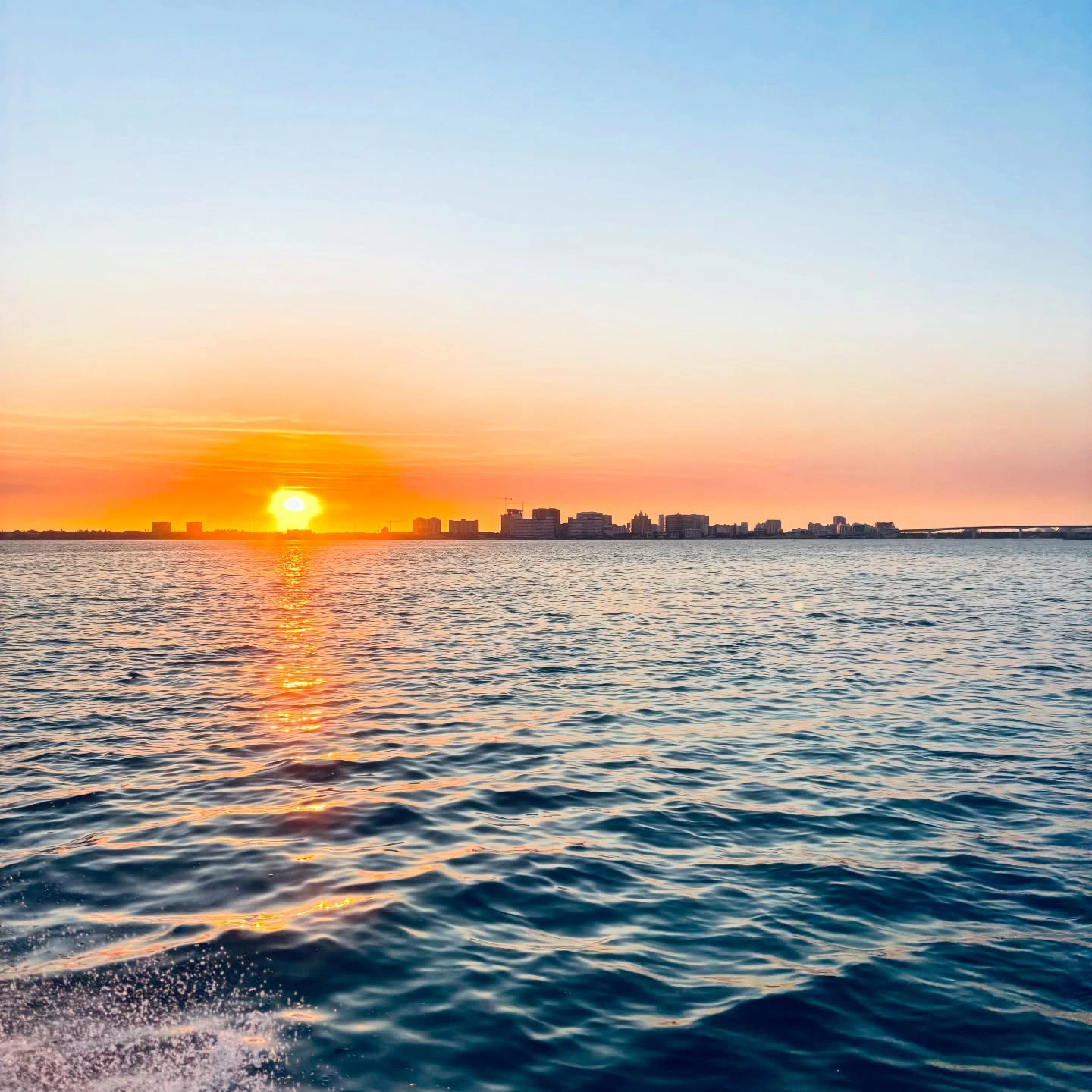 Golden sunset over Sarasota Bay with calm blue water and the Sarasota skyline in the distance.