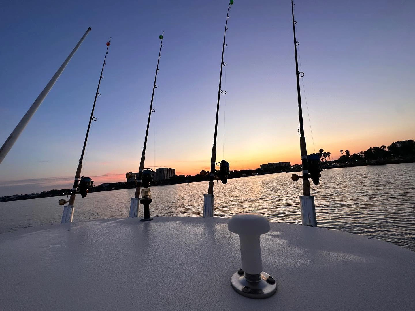 Fishing rods aboard a Sarasota fishing charter boat at sunset overlooking calm waters and the Sarasota skyline.