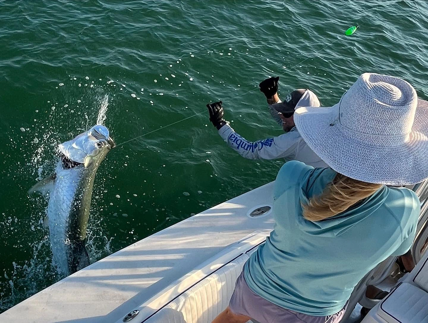 Young angler fishing from the bow of a Sarasota fishing charter boat while a captain records the moment during sunset.