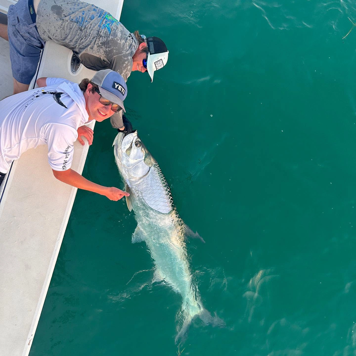 Young angler and captain carefully releasing a large tarpon beside a Sarasota fishing charter boat after a successful catch.