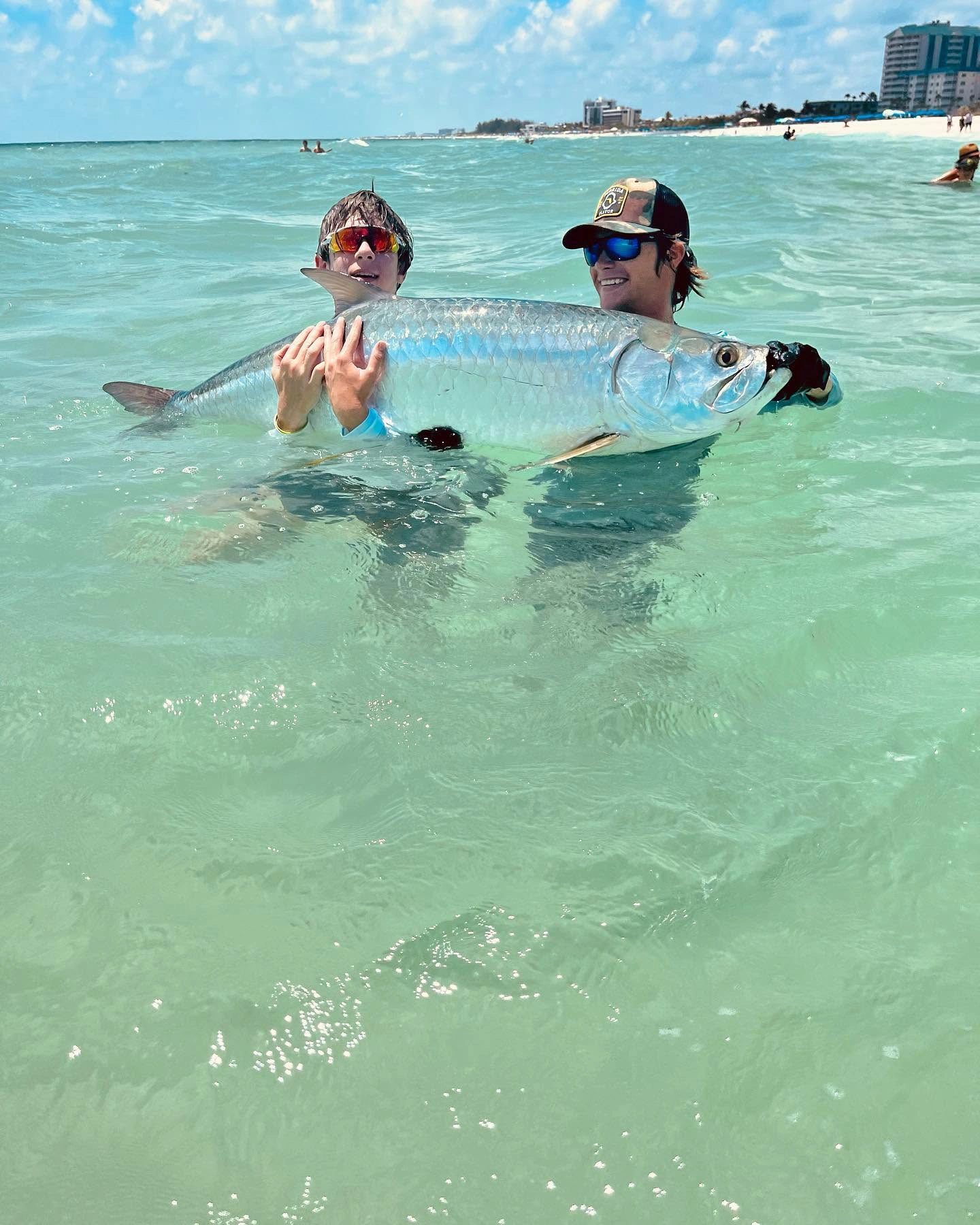 Two young anglers holding a large tarpon in shallow water during a Sarasota fishing charter before releasing the fish.