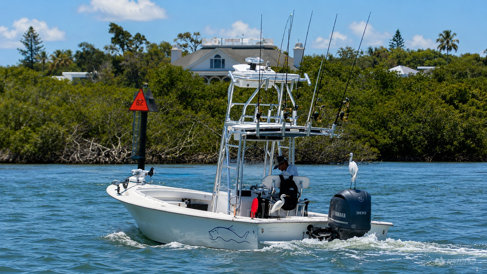 Center console fishing boat cruising through Sarasota Bay with a tower, multiple fishing rods, and two white egrets perched aboard.