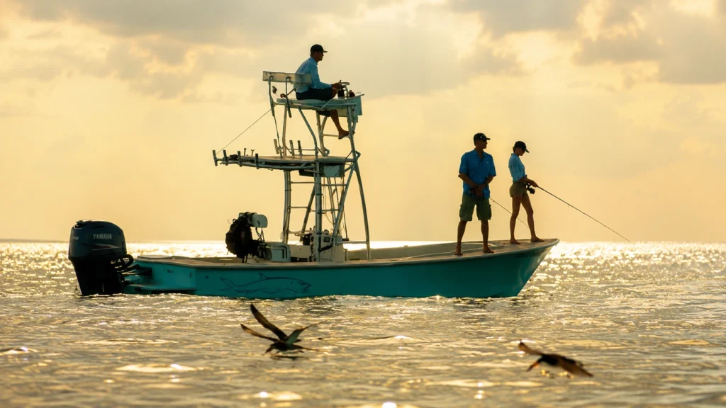 Anglers fly fishing from a technical poling skiff during sunrise on Sarasota Bay.